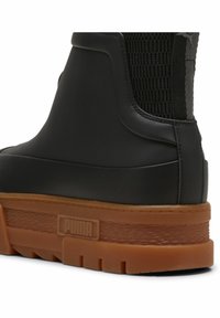 Zwarte rubberen laars met een getextureerd achterpaneel en een stevige gumzool. Het heeft een logodetail op de hak en een gladde afwerking.