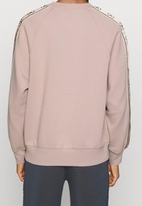 Sweatshirt rose clair à col rond avec des poignets et un ourlet côtelés, doté d'une décoration de marque le long des coutures des épaules. Tissu à texture douce.