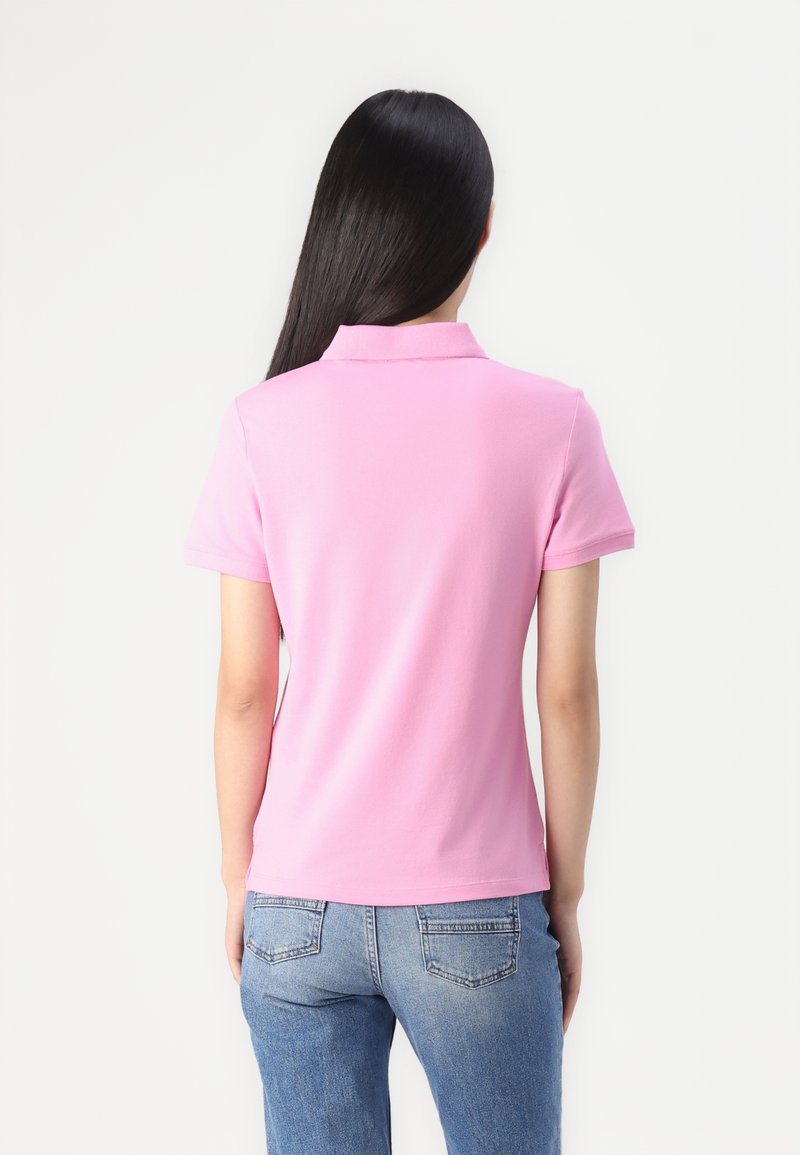 Rosa Polohemd mit kurzen Ärmeln und Kragen, aus glattem Stoff gefertigt. Verfügt über ein tailliertes Design und einen geraden Saum. Getragen mit blauen Jeans.