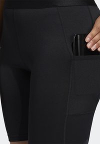 Shorts de sport noirs à coupe ajustée, avec une poche latérale contenant un smartphone. Le matériau est lisse, avec des détails de couture visibles.