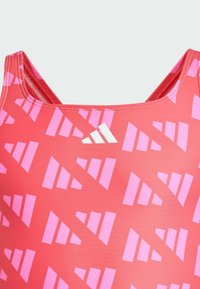 Red swimming suit with a geometric pink pattern. Features a wide neck, thick straps, and a white logo on the upper left side. Smooth texture.