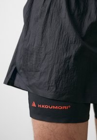 Svarta sportshorts med perforerade paneler, med resårmidja. Inkluderar svarta kompressionsshorts under med orangea loggdetaljer.