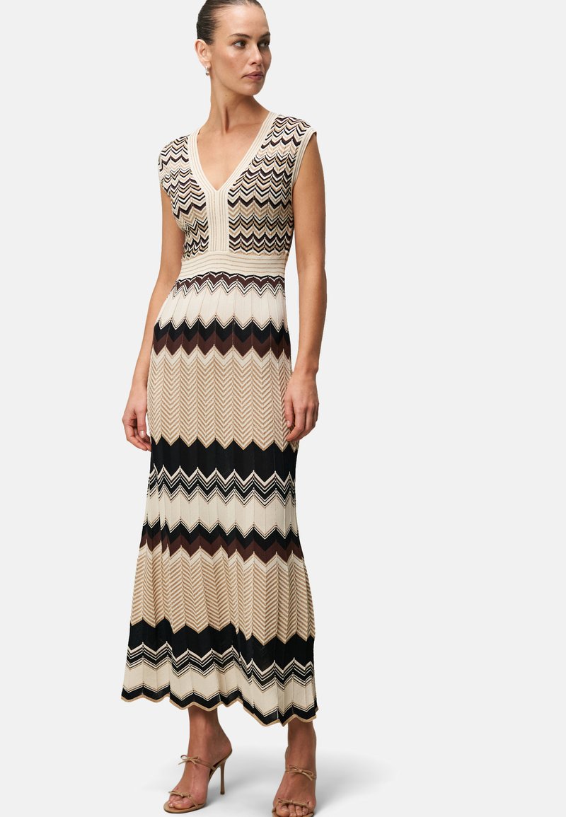Knit maxi dress featuring a deep V-neck and cap sleeves. Chevron pattern in beige, black, and brown with a fitted waist and flared skirt.