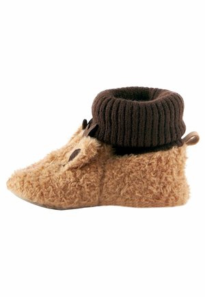 Miękkie jasnobrązowe kapcie z detalem w postaci twarzy zwierzęcia oraz ciemnobrązowym prążkowanym mankietem z dzianiny, zaprojektowane dla zapewnienia ciepła i wygody.
