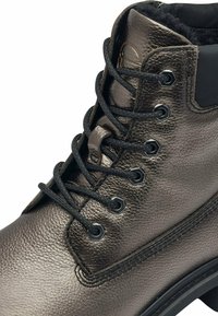 Botín de cuero gris metálico hasta el tobillo con cordones negros, punta redonda y superficie texturizada. Presenta ojales metálicos y forro de forro polar.
