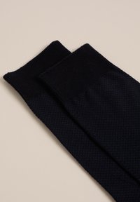 Stickade marinblå strumpor med ett strukturerat mönster och ribbad manschett visas sida vid sida på en ljus bakgrund.