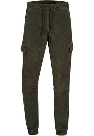 Mann trägt dunkelgrüne Cargo-Jogginghosen mit Kordelzug in der Taille und elastischen Bündchen, kombiniert mit weißen Sneakers und einem weißen Hemd.