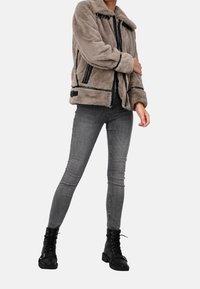 Grå jacka i fuskpäls med krage, svarta dragkedjor och detaljer. Kombinerad med grå skinny jeans och svarta snörstövlar.