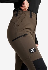 Bruna funktionella byxor med svarta accenter, med ett elastiskt midjeband, sidoficka med dragkedja och en märkespatch på låret.