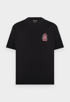 T-shirt noir à manches courtes avec col rond et un petit écusson brodé rouge et blanc sur le haut gauche de la poitrine.