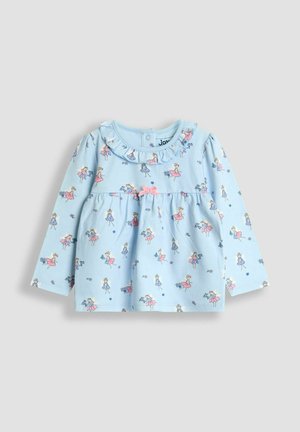 Haut pour bébé à manches longues bleu clair avec de petites imprimés de fées, un col volants, et un nœud rose au centre de la poitrine.