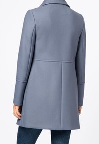 Cappotto in lana grigio chiaro strutturato con collo con revers, maniche lunghe e taglio dritto. Presenta una sottile trama diagonale e un dettaglio con cucitura posteriore.