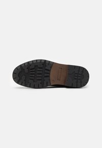 Suola di scarpa in gomma nera con motivo di battistrada testurizzato; area di accento marrone con logo, progettata per aderenza e durata.