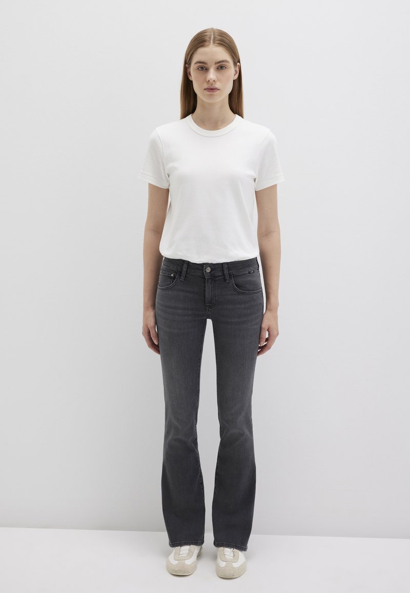 T-shirt bianca in cotone abbinata a jeans flare in denim grigio scuro a taglio slim. L'outfit è completato da sneakers di colore chiaro. Design e vestibilità semplici.