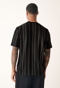 Schwarz gestreiftes Kurzarmhemd aus strukturiertem Stoff mit weißen vertikalen Streifen, rundem Ausschnitt und lockerem Schnitt.