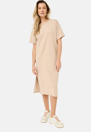 Beige cotton t-shirt dress with short sleeves, a round neck, side slit, and a relaxed fit, paired with chunky white sneakers with pastel accents.