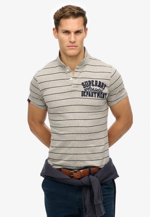 Grå polo shirt med marineblå striber, krave med to knapper og lille broderet logo på brystet. Bæres med marineblå bukser og brunt bælte.
