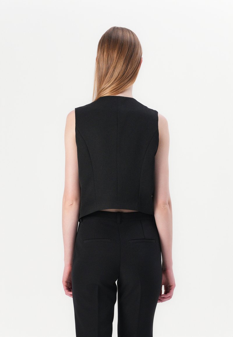 Haut sans manches noir avec un design structuré, coupe courte et tissu texturé. Associé à un pantalon noir ajusté avec des poches arrière.