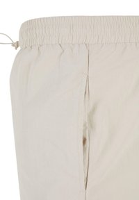 Beige bukser med elastisk liv og snor, med en sidelomme og glat stofstruktur.