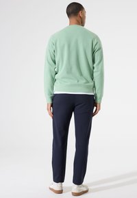 Mintgroene sweatshirt met een ronde hals en ribgebreide mouwen, gecombineerd met marineblauwe tapered broeken en witte sneakers. Minimalistisch ontwerp.