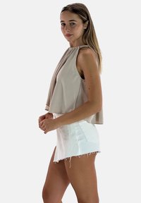 Top senza maniche beige chiaro con tessuto drappeggiato; abbinato a una mini gonna in denim bianca con orlo sfilacciato. Tessuto liscio e vestibilità rilassata.