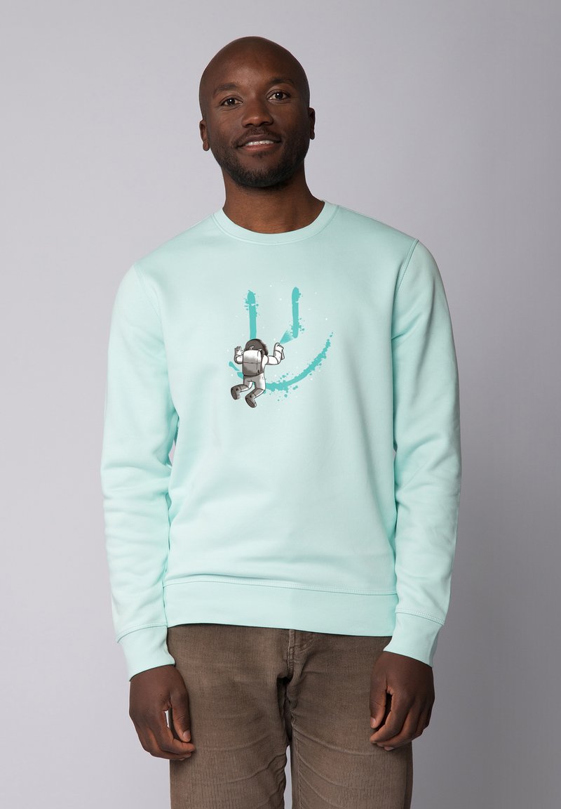 Sweatshirt vert menthe avec un col rond et des manches longues, présentant un graphisme d'un astronaute et des éclaboussures de peinture teal.