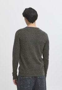 Pulover verde tricotat cu mâneci lungi și guler rotund. Textură moale, design ajustat și un model subtil pe spate.