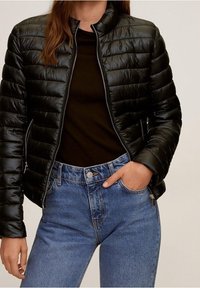 Sort pufferjakke med kviltet tekstur og høj krave, parret med en mørk top og højtaljede blå jeans med knaplukning.