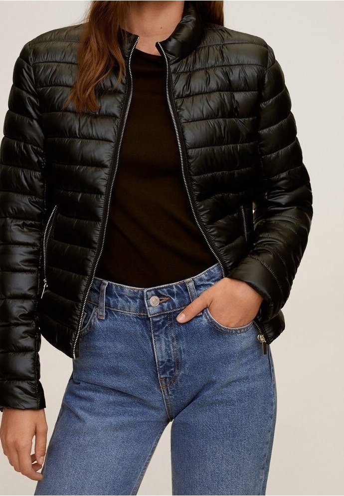 Sort pufferjakke med kviltet tekstur og høj krave, parret med en mørk top og højtaljede blå jeans med knaplukning.