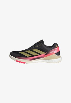 Scarpa sportiva nera con strisce dorate, accenti rosa, suola bianca e tomaia in mesh, progettata per la corsa e attività sportive.