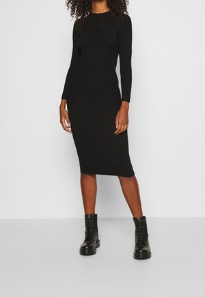 Robe en maille côtelée noire avec manches longues, silhouette ajustée et ourlet à hauteur du genou, associée à des bottes de combat noires lacées.