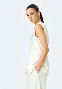 Ärmelloses weißes Top aus einem weichen Stoff, mit lockerer Passform und einem taillierten Bund. Verfügt über eine Seitentasche und ein glattes, minimalistisches Design.