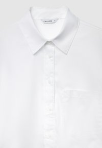 White button-up shirt with a classic collar, made from smooth fabric. Features a front pocket and plastic buttons. Tag reads "CALLIOPE S."