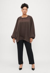Brązowa, zwiewna bluzka z okrągłym dekoltem i długimi, marszczonymi rękawami, w połączeniu z czarnymi, prostymi spodniami i czarnymi szpilkami.