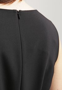 Detailní záběr na záda osoby, která má na sobě černý bezrukávový oděv se zipem u horní části.