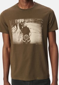 Camiseta de algodón verde oliva con una impresión fotográfica vintage de peatones y un motociclista en la parte delantera. Diseño de cuello redondo.