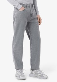 Jean en denim gris avec une coupe straight leg, dotés de poches avant et arrière, assortis à des chaussures de sport gris clair.