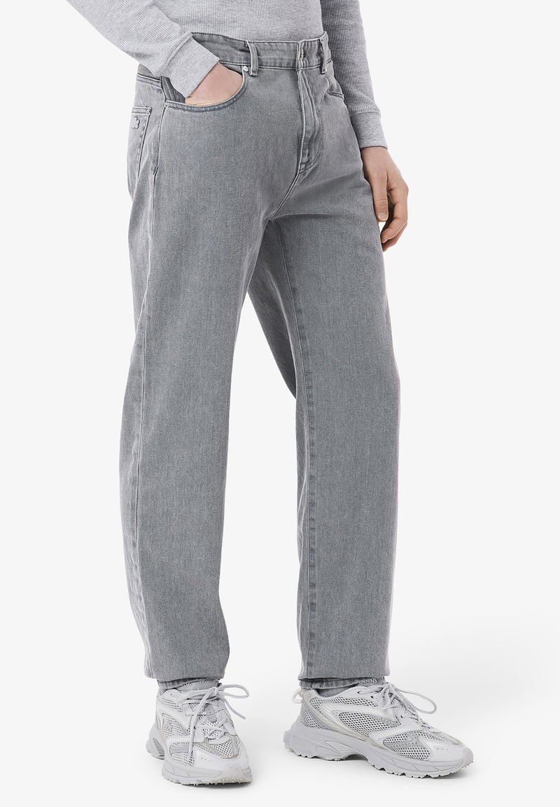 Jean en denim gris avec une coupe straight leg, dotés de poches avant et arrière, assortis à des chaussures de sport gris clair.