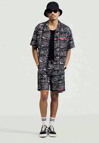 T-shirt med kort ärm i svart och vitt med grafiskt tryck, matchande shorts, lättviktigt material, abstrakta mönster, kombinerat med vita sneakers och en svart bucket hat.