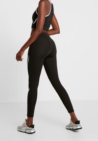 Black athletic leggings with a high waist, featuring white side accents and a smooth texture. Paired with a black crop top and silver shoes.