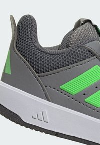 Szary but sportowy z teksturowaną cholewką z siateczki, zielonymi akcentami oraz białą śródstopiem z wyraźnym bieżnikiem.