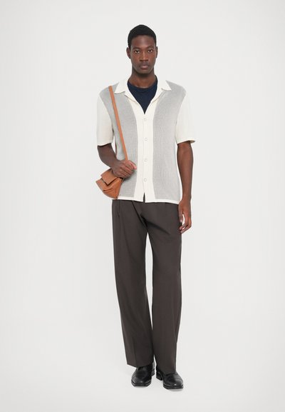 Short-sleeve, button-up shirt with a textured light grey and cream pattern, paired with dark brown trousers and a brown crossbody bag.