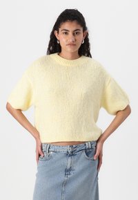 Gul strikkegenser med korte ermer og rund hals, kombinert med en høy midje blå denimskjørt. Myk tekstur med en avslappet passform.