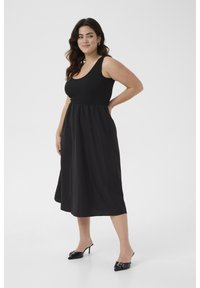 Zwarte maxi-jurk met een aansluitende geribbelde bovenkant en een vloeiende rok. Gladde stof met een gegatherde taille naad. Gepaard met zwarte hoge mules.