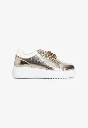 Metalické zlaté tenisky s bílými akcenty, texturovaný svršek, ploché tkaničky a dekorativní ozdoby na jazyku. Gumová podrážka.