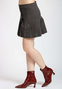 Gonna grigia a pieghe con chiusura a bottoni, abbinata a stivaletti rossi lucidi con punta appuntita e tacco basso, su sfondo neutro.