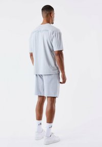 Camiseta de algodón gris claro con mangas cortas, combinada con pantalones cortos gris claro. Zapatillas blancas y calcetines con diseño de acento completan el look.