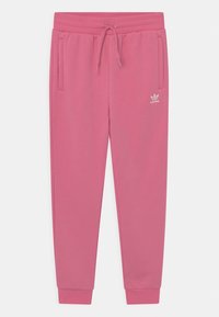 Růžové tepláky vyrobené z měkké tkaniny, s pásem na šňůrku, dvěma bočními kapsami a bílým logem na levém stehně.