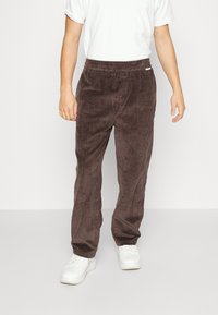 Hnědé manšestrové kalhoty s texturovanou tkaninou, elastickým pasem a přímým střihem, doplněné o bílé tenisky.