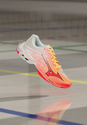 Chaussure de sport légère blanche, orange et rouge avec des lacets jaunes, flottant au-dessus d'un sol de gymnase avec des lignes de terrain.